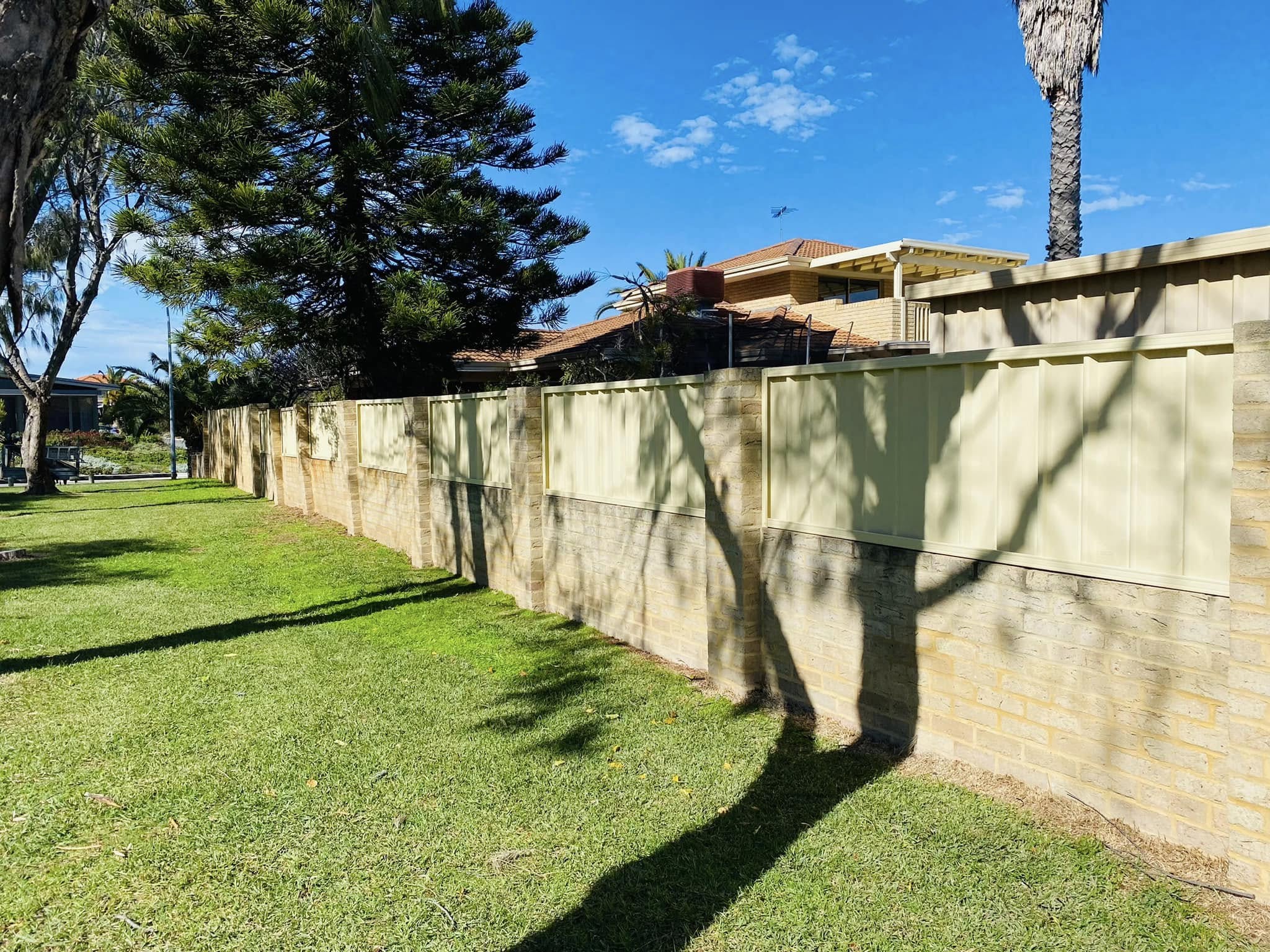 Cream Colorbond infill fence on a limestone boundary wall along a verge