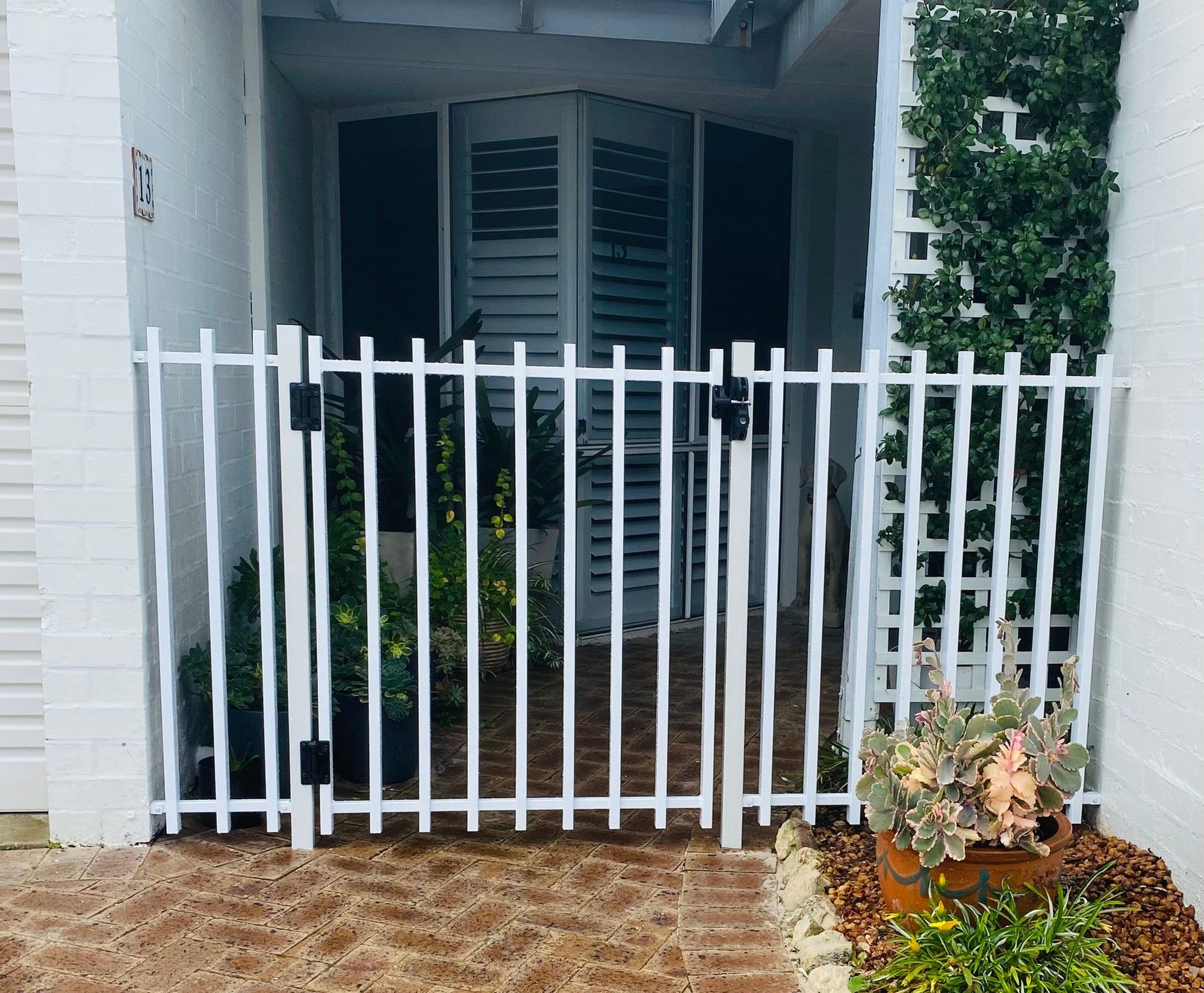 White aluminium tubular pedestrian gate installed at a home entrance with garden and trellis
