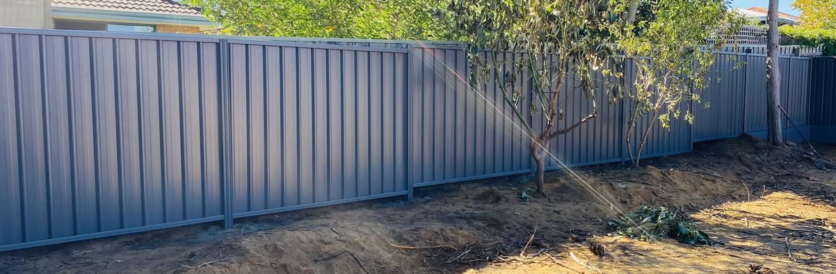 Slate-grey Colorbond boundary fence freshly installed beside an established tree