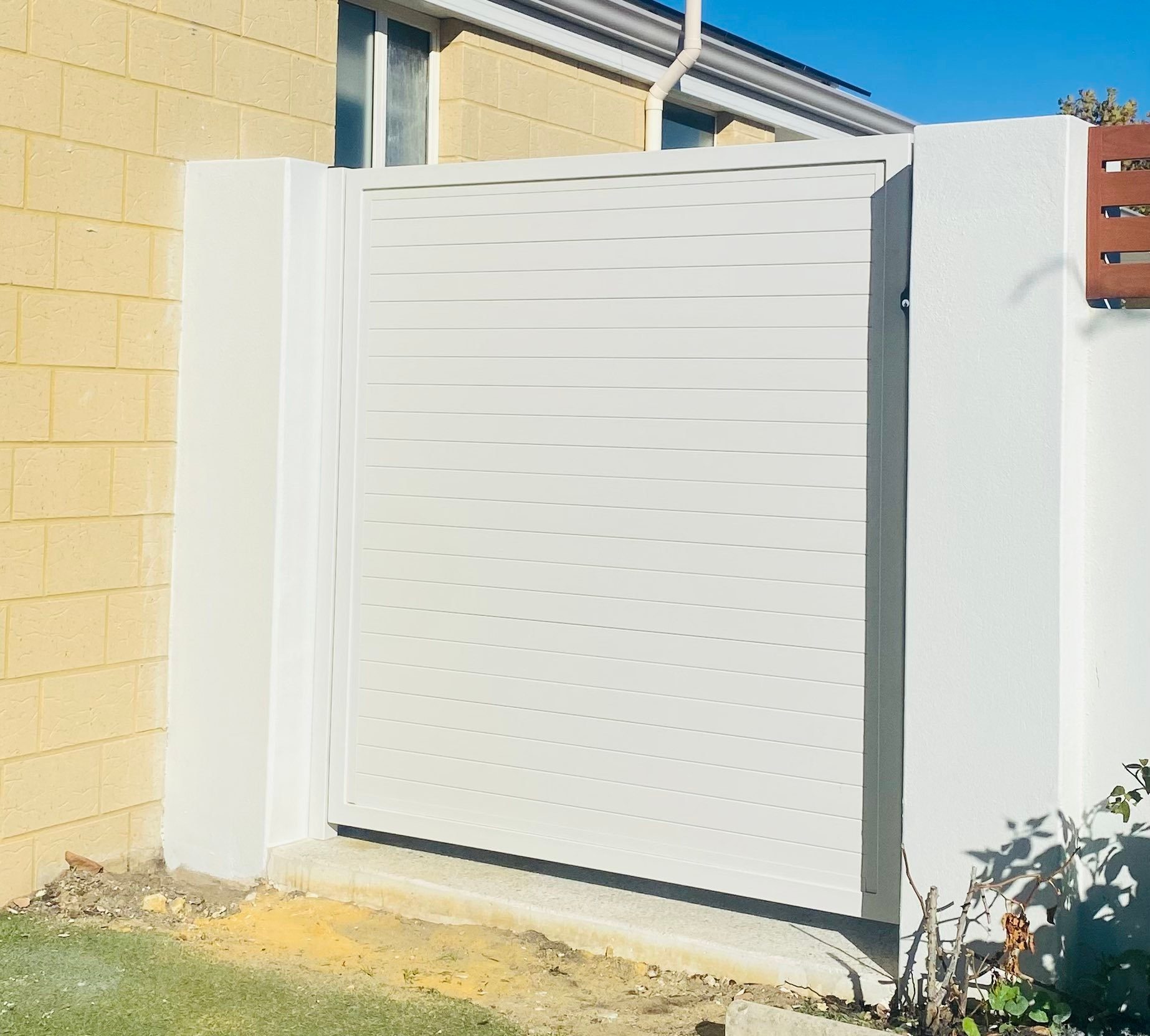White horizontal-slat aluminium gate set into a rendered boundary wall