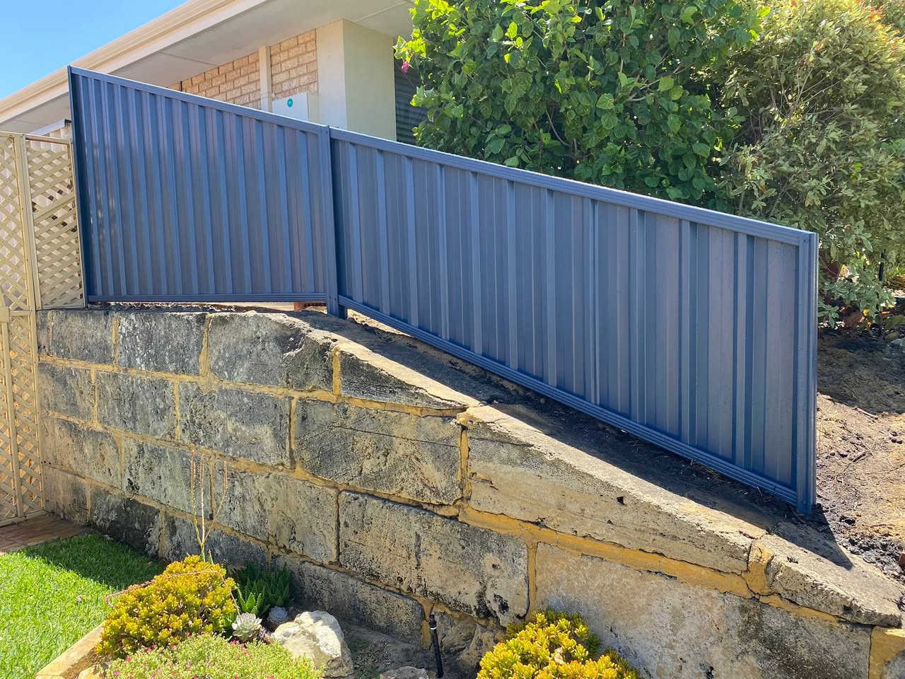 Slate-grey Colorbond fence panels installed along a limestone retaining wall at a Perth northern-suburbs home
